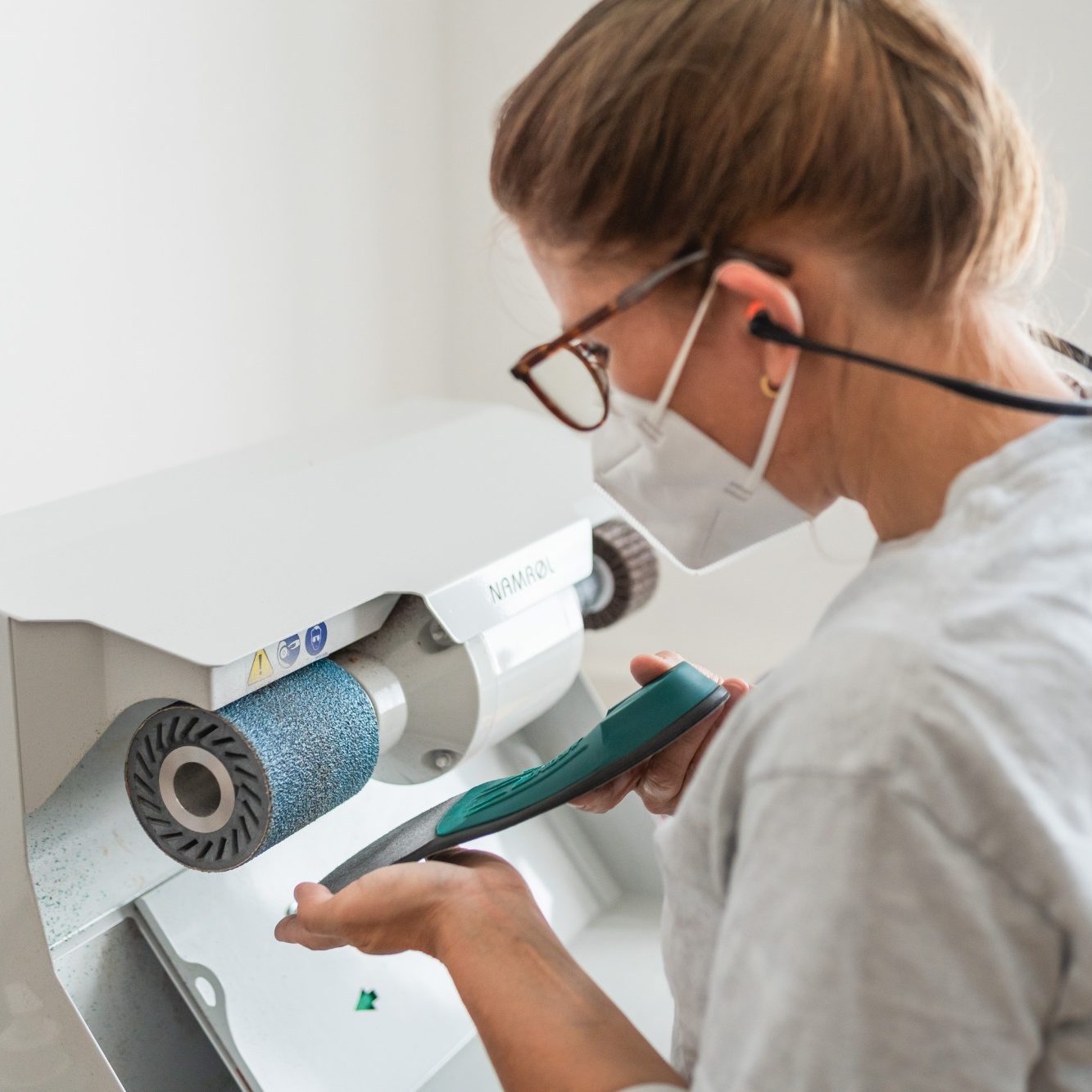 Die Technikerin schleift die Einlage an der Schleifmaschine.